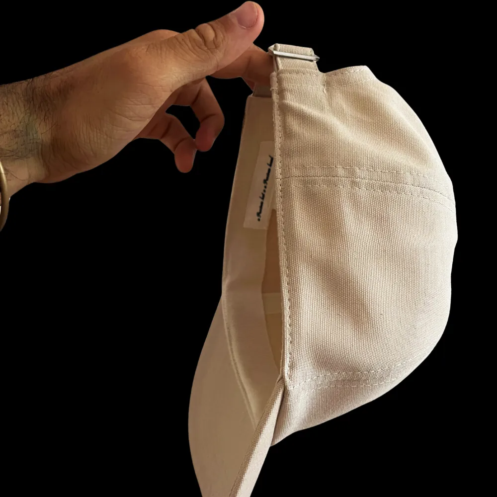 Cappello NSOC visto di lato, tenuto in mano: profilo pulito senza occhielli